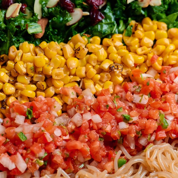 Close-up of a colorful salad with rows of kale, corn, pico de gallo, and noodles.
