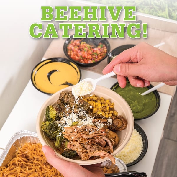 Hands holding a bowl of Beehive Catering food, adding cheese, with other dishes in the background.