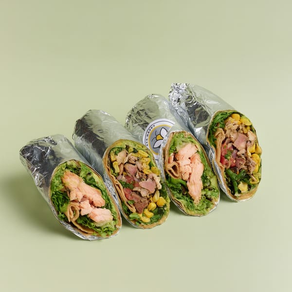 Four Bee Happy wraps, two with salmon and two with chicken and corn, on a light green background.